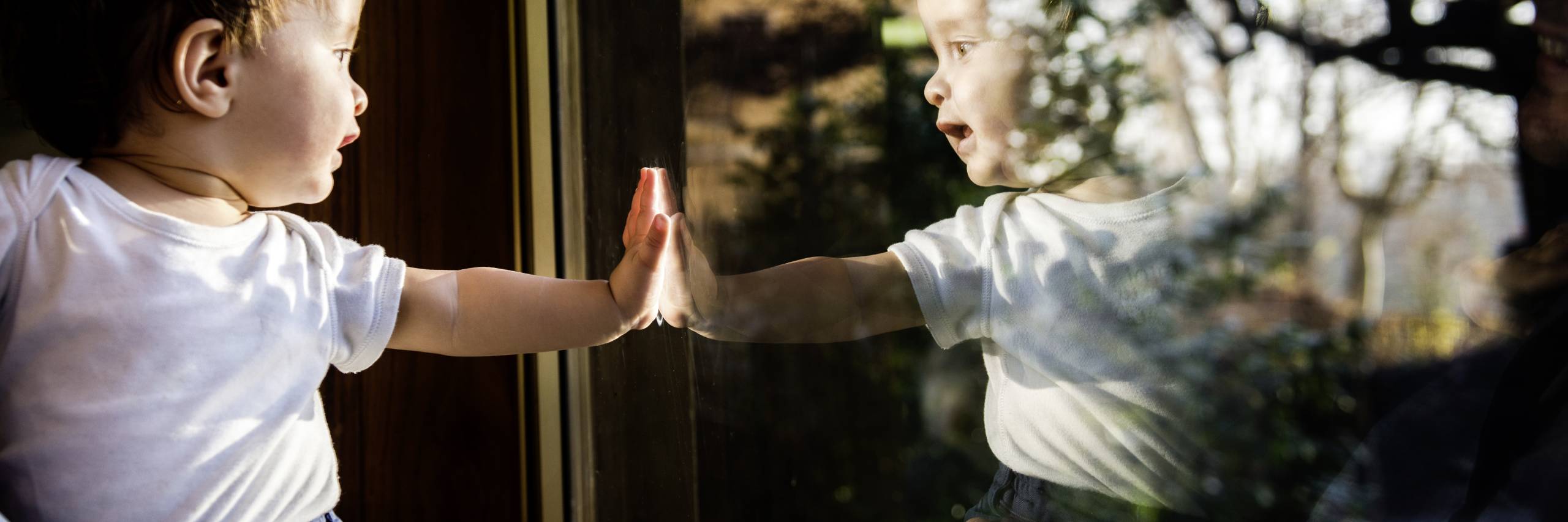 Baby boy in fathers arms looking through and touching window
