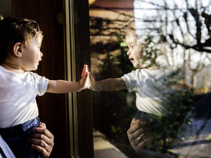 Baby boy in fathers arms looking through and touching window