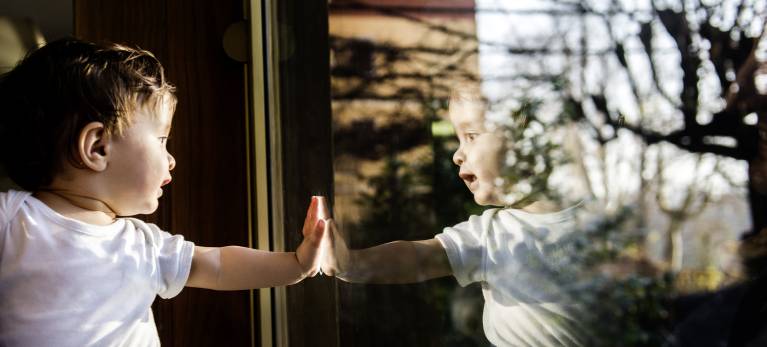 Baby boy in fathers arms looking through and touching window